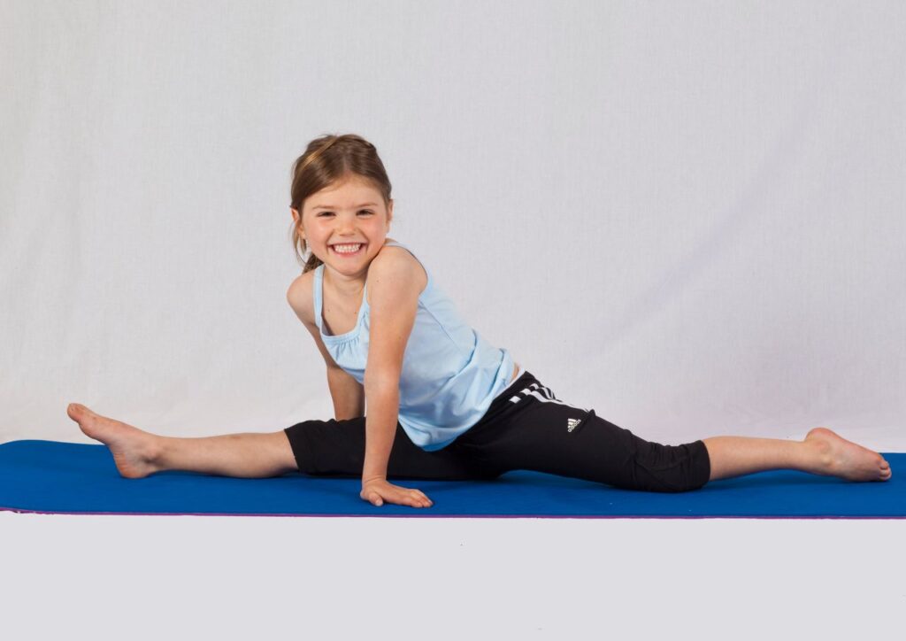 pexels-photo-3992601-3992601 Smiling young girl performing a split on a yoga mat indoors, showcasing flexibility and joy in exercise.